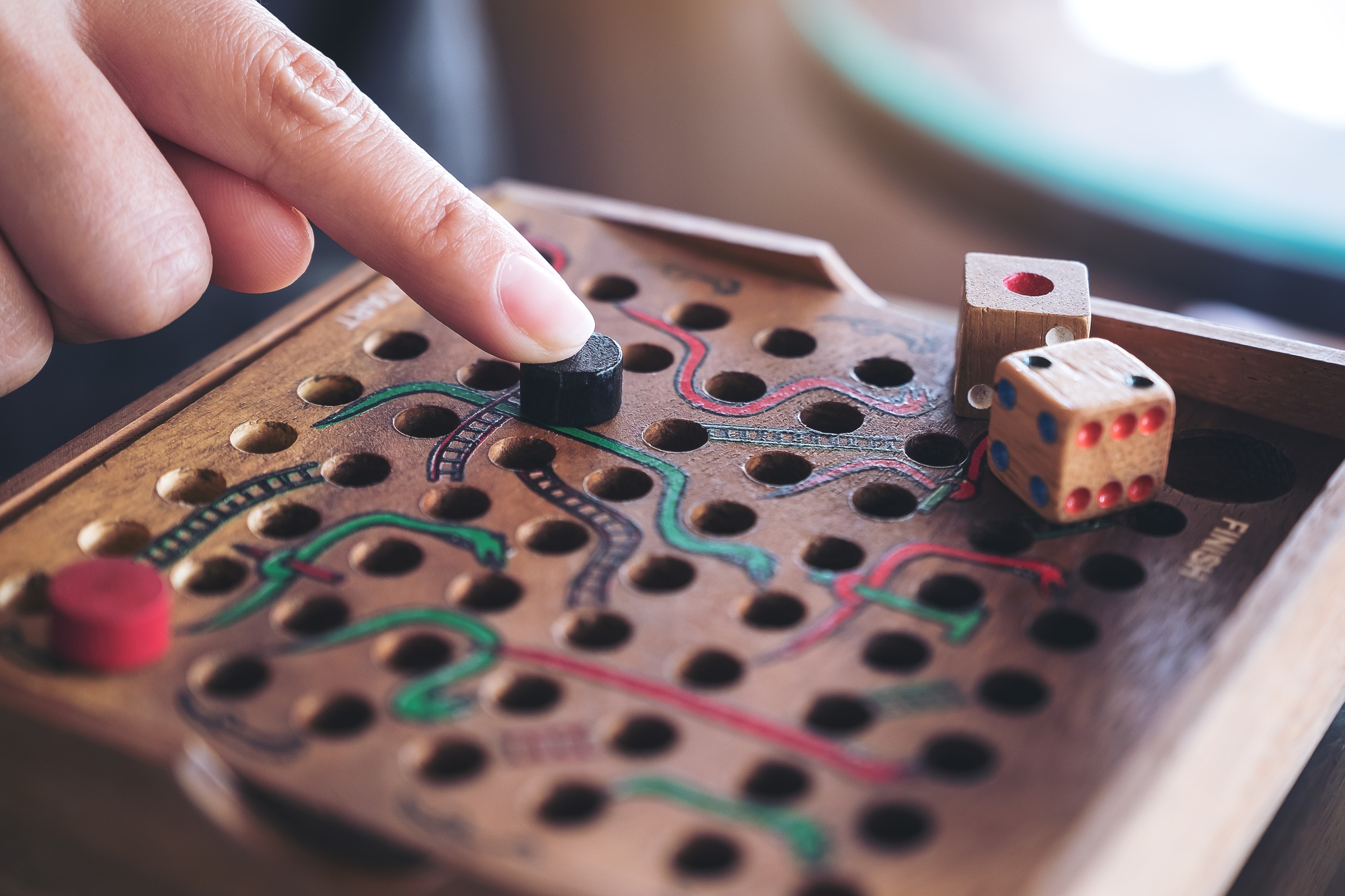 Closeup image of a hand playing wooden Snakes and Ladders game